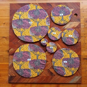 May include: A set of nine round, reusable food covers in various sizes. The covers are made of fabric with a yellow background and a pink and gray floral pattern. The covers are labeled with their sizes: XS, 2XS, 3XS, S, M, L, XL, 2XL, and 3XL.