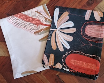 Könnte beinhalten: Zwei Geschirrtücher mit Blumendesigns. Eines ist weiß mit einem roten und orangefarbenen Blumendesign. Das andere ist schwarz mit einem braunen und orangefarbenen Blumendesign.