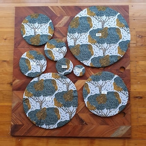 May include: A set of 9 round placemats with a white background and a repeating pattern of blue and gold trees. The placemats are labeled with sizes: XS, 2XS, 3XS, S, M, L, XL, 2XL.