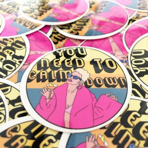 May include: A stack of round stickers with a yellow background and a woman in a pink robe holding a cocktail. The text on the sticker reads "You Need To Calm Down".