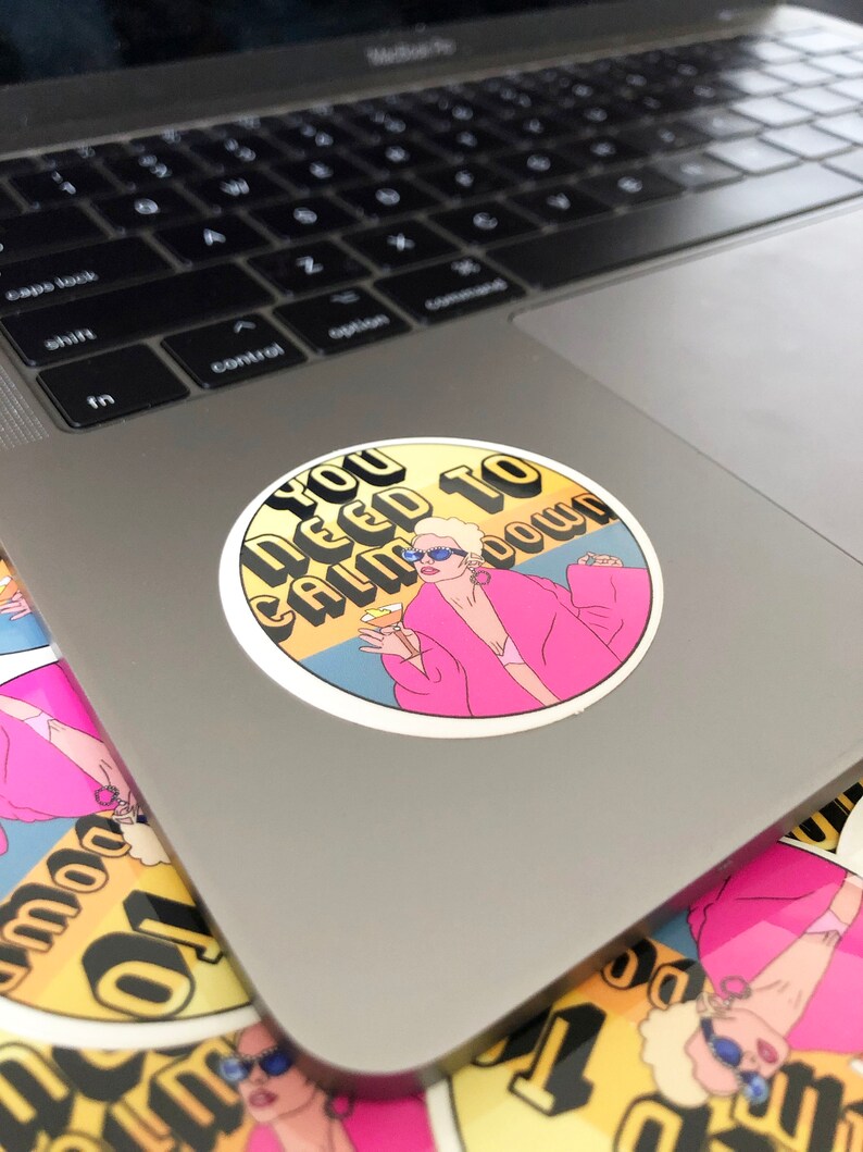 May include: A round sticker with a yellow background and the text "You Need To Calm Down" in black and white letters. A cartoon illustration of a woman with blonde hair wearing a pink robe and sunglasses is holding a glass of champagne.