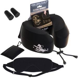 May include: Black travel pillow kit with a neck pillow, eye mask, earplugs, and a small pouch. The neck pillow has a zipper and a strap. The eye mask has a strap. The pouch has a zipper and a carabiner clip. The kit includes the text "Flying Monkey" and "Luxury Travel Pillow".