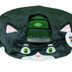 May include: Black and white plush cat-shaped cover for a robot vacuum cleaner. The cover has green eyes and a pink nose. The vacuum cleaner is visible through the opening in the cover. The cover has a tag that says "Roro Raccoon" and "www.rororaccoon.com".