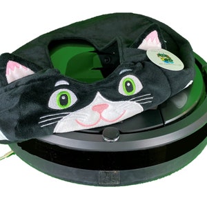 May include: Black and white cat-shaped plush cover for a round, black robot vacuum cleaner. The cover has green eyes and a pink nose.