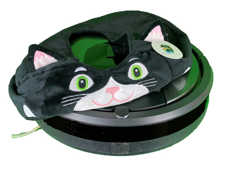 May include: Black and white cat-shaped plush cover for a round, black robot vacuum cleaner. The cover has green eyes and a pink nose.