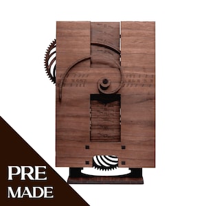 Pode incluir: Um relógio de parede de madeira com acabamento castanho escuro. O relógio apresenta uma engrenagem, um design em espiral e uma janela retangular que exibe números. As palavras "PRE MADE" são impressas no canto inferior esquerdo.
