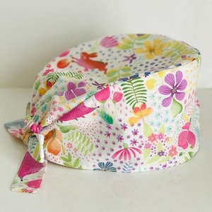 May include: A white scrub hat with a colorful floral and animal print. The hat has a pink tie that can be tied at the back of the head.