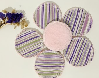 May include: A collection of reusable facial rounds. Five rounds feature a striped pattern in purple, green, and white. One round is solid pink. The rounds are arranged in a flower-like shape.