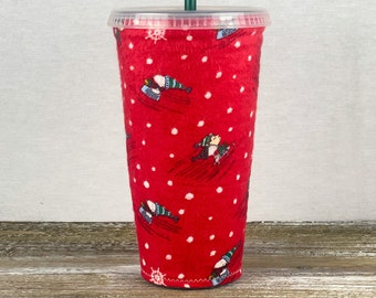 May include: Red reusable cup with a white polka dot pattern and a design of penguins ice skating. The cup has a clear plastic lid.