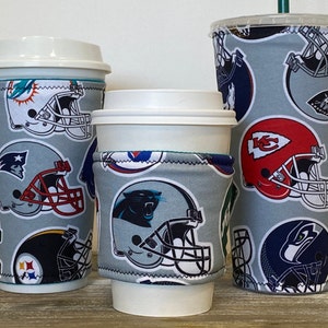 May include: Three insulated coffee cup sleeves with a gray background and a pattern of different NFL team logos. The logos include the New England Patriots, Kansas City Chiefs, Seattle Seahawks, Pittsburgh Steelers, Carolina Panthers, and Miami Dolphins.