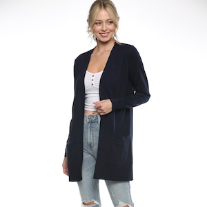 May include: A navy blue long-sleeved cardigan with pockets. The cardigan is open and worn over a white tank top and light blue jeans. The person is wearing white sneakers.