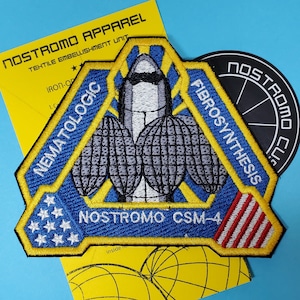 Puede incluir: Parche bordado con un diseño azul, amarillo y blanco con el texto "NEMATOLOGIC FIBROSYNTHESIS NOSTROMO CSM-4". Una tarjeta amarilla con el texto "NOSTROMO APPAREL" está detrás del parche. También es visible una pegatina circular negra.