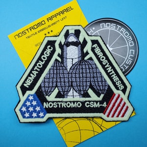 May include: A black triangular patch with a white alien figure in the center. The patch has the text "NOSTROMO CSM-4" in white, "NEMATOLOGIC" in white on the left side, and "FIBROSYNTHESIS" in white on the right side. The patch has a red, white, and blue American flag on each side.