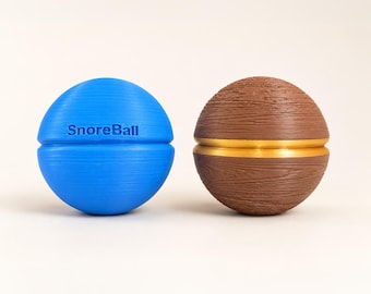 Könnte beinhalten: Ein hellblaues kugelförmiges Objekt mit dem eingeprägten Text SnoreBall auf der Oberfläche, neben einem braunen kugelförmigen Objekt mit Holzmaserung und einem horizontalen goldenen Band, das durch die Mitte beider Objekte verläuft.