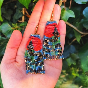 May include: A pair of beaded earrings with a red, black, green and blue floral design. The earrings are hanging from gold hooks.