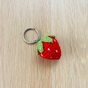 May include: A red crocheted strawberry keychain with green leaves and a silver key ring.
