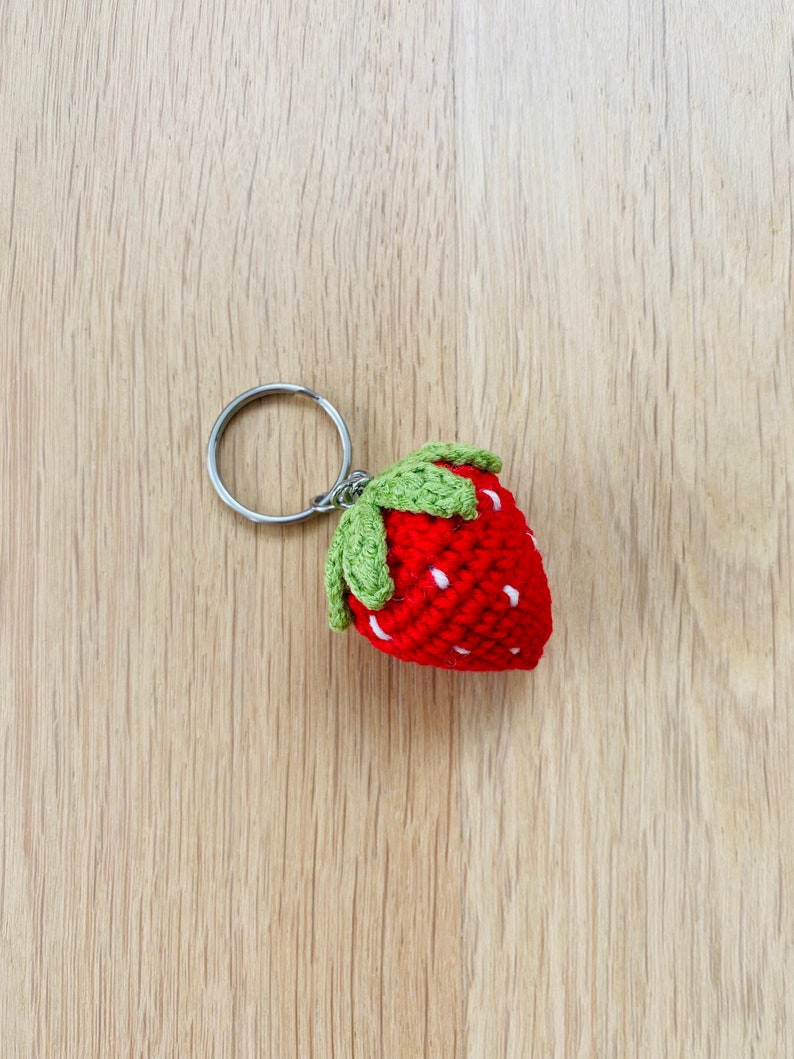 May include: A red crocheted strawberry keychain with green leaves and a silver key ring.