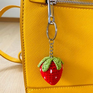 May include: A yellow handbag with a zipper closure and a crocheted strawberry keychain attached to the zipper pull.