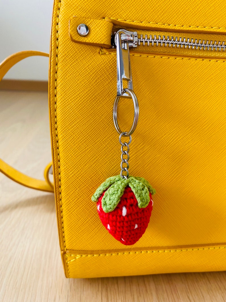 May include: A yellow handbag with a zipper closure and a crocheted strawberry keychain attached to the zipper pull.