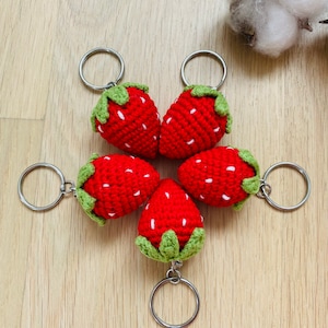 May include: Five crocheted strawberry keychains with green leaves and white stitching. Each keychain is attached to a silver key ring.