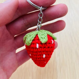 May include: A red and green crocheted strawberry keychain with white accents. The strawberry is attached to a silver key ring.