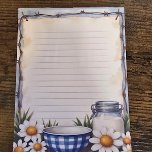 May include: Lined notepad with a rustic design. Features a blue and white checkered bowl, a jar of milk, and daisies. The notepad has a barbed wire border and a light blue background.