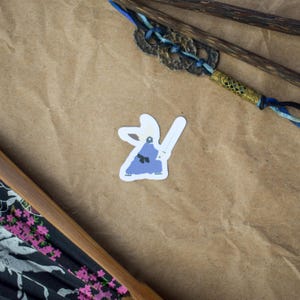 Pu&ograve; includere: Un adesivo con una figura vestita di blu che tiene una spada, su sfondo bianco.
