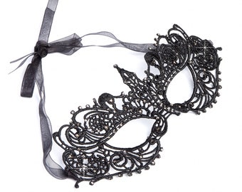 Puede incluir: Una máscara de encaje negro para el baile de máscaras con pedrería y un lazo negro.