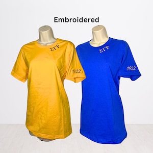 May include: Two embroidered t-shirts, one yellow and one blue, with the letters "ΣΤΡ" and the number "1922" on them.