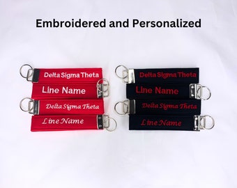 May include: A set of red and black keychains with the text "Delta Sigma Theta" and "Line Name" embroidered on them. The keychains are made of fabric and have silver metal rings.