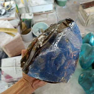 Pode incluir: Um grande pedaço de vidro de forma irregular, azul escuro, com uma superfície lisa e brilhante. O vidro tem um leve tom marrom e parece translúcido.