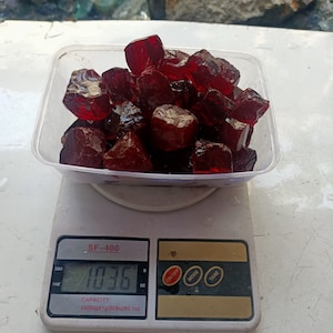 Puede incluir: Una báscula digital que muestra 10,36 onzas con un recipiente blanco lleno de piedras preciosas rojas. La báscula indica "SF-400" y tiene una capacidad de 10000g x 1g / 353oz x 0.1oz.