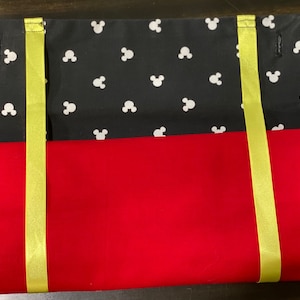 May include: A red and black fabric pencil case with yellow straps. The black fabric has a white Mickey Mouse head pattern.