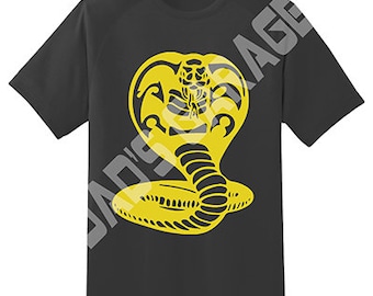 May include: Black t-shirt with a yellow cobra graphic. The cobra is in a striking pose with its head raised and fangs bared.