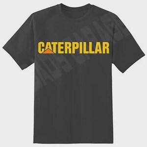 May include: Dark gray t-shirt featuring the word "CATERPILLAR" in yellow block letters with a yellow and orange logo. The shirt has short sleeves and a crew neck.