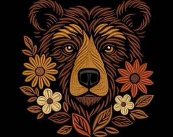May include: Embroidered bear face with floral accents. The bear is depicted in shades of brown, tan, and gold, with a black nose and eyes. The flowers are in shades of yellow, orange, and cream, surrounded by brown leaves, all set against a black background.