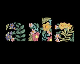 May include: Embroidered floral design spelling out the word "ala" in a stylized font. The letters are filled with colorful flowers and leaves in shades of purple, pink, yellow, and green, set against a black background.