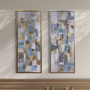 Op de afbeelding: Twee abstracte schilderijen in gouden lijsten, elk met een geometrisch patroon van witte, grijze en blauwe vierkanten en rechthoeken. De schilderijen hangen aan een muur met bruine lambrisering.