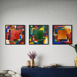 Pode incluir: Três pinturas abstratas emolduradas com formas geométricas coloridas e uma moldura preta. As pinturas estão penduradas em uma parede de tijolo branco sobre uma prateleira azul escura com uma cadeira branca e um banquinho preto.