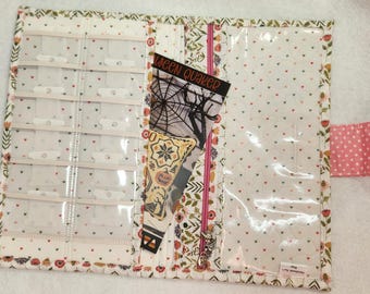 May include: A white fabric zippered pouch with a clear plastic window. The pouch has a floral pattern with small red hearts. The pouch is open and has a card inside that says "Halloween Quaker".