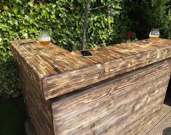 May include: A rustic wooden bar with a dark brown finish. The bar has a corner design and a top surface with two glasses of beer on it. The bar is made of reclaimed wood and has a natural, weathered look.