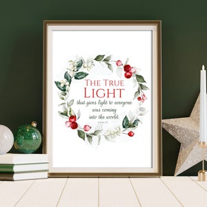 Puede incluir: Una impresión enmarcada con el texto "THE TRUE LIGHT" rodeada por una corona de acuarela de hojas verdes, bayas blancas y bayas rojas. Dos velas blancas y una decoración en forma de estrella están a la derecha.