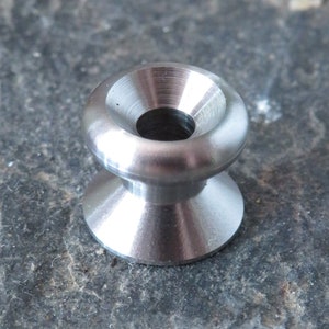 May include: A silver metal eyelet with a smooth, rounded surface and a central hole. The eyelet is designed for use in leather goods, fabric, or other materials.