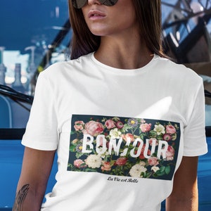 Puede incluir: Camiseta blanca con estampado floral y el texto "Bonjour La Vie est Belle".