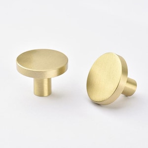 May include: Two brushed brass cabinet knobs with a round top and a cylindrical base.