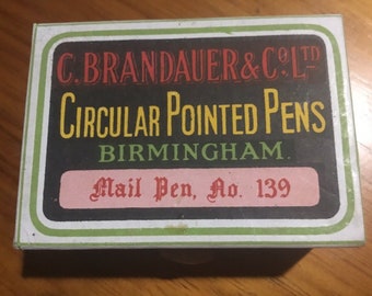Könnte beinhalten: Eine Vintage-Blechdose für C. Brandauer & Co. Ltd. Rundspitzen-Federn, hergestellt in Birmingham. Die Dose ist grün, weiß und schwarz mit roten und gelben Schriftzügen. Auf einem rosa Etikett steht "Mail Pen, No. 139".