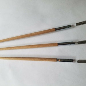 Pode incluir: Três porta-canetas de caligrafia com cabos de madeira e pontas de metal. As pontas estão separadas dos porta-canetas. As canetas estão dispostas horizontalmente sobre um fundo branco. As canetas são feitas para escrever e desenhar.