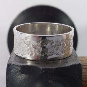 Può includere: Un anello d'argento con una finitura martellata testurizzata. L'anello è appoggiato su un'incudine di metallo nero.