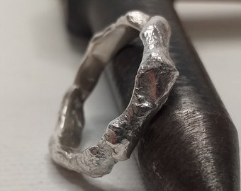 Könnte beinhalten: Ein silberner Ring mit einer rauen, strukturierten Oberfläche. Der Ring liegt auf einem Metallwerkzeug.