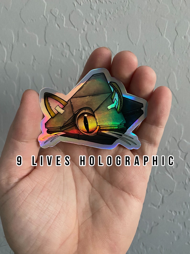 May include: A holographic sticker of a cat with a large eye and a geometric design. The sticker is iridescent and has the text "9 LIVES HOLOGRAPHIC" printed below it.